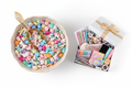 Bowl of multicoloured charm beads in dragonfly, paw print, unicorn and heart shapes with a golden scoop spoon, next to a gift box of prizes